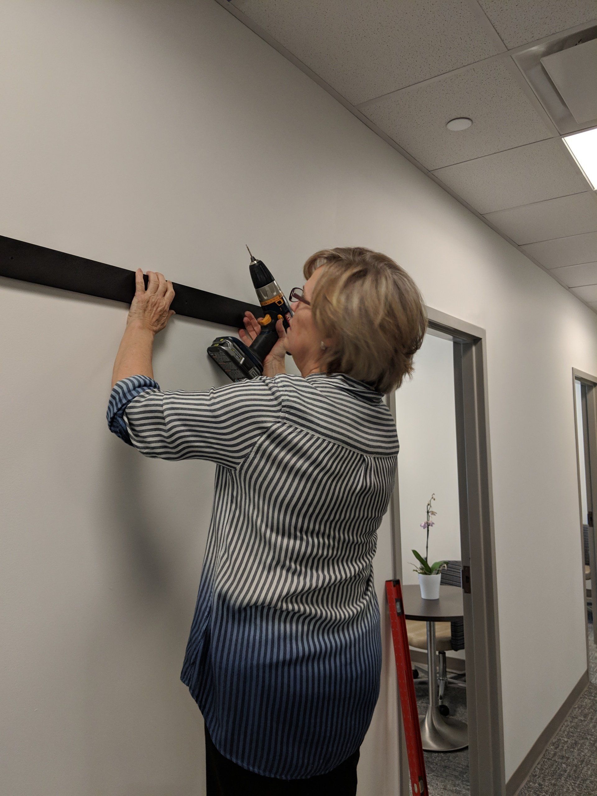 A woman is working on a wall with a drill.
