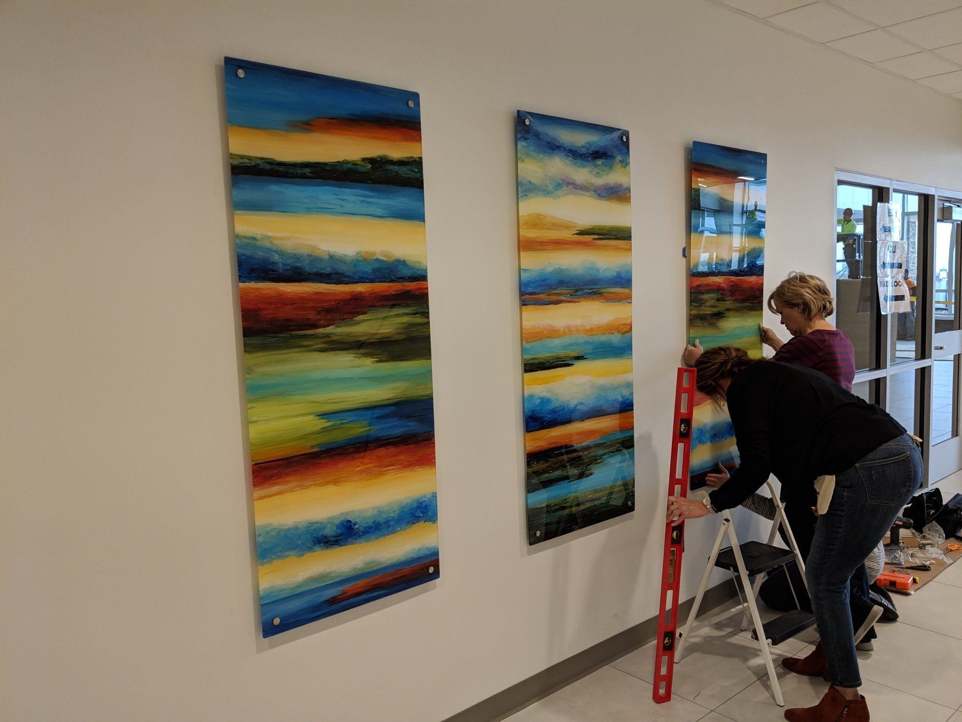 A couple of people are hanging paintings on a wall.