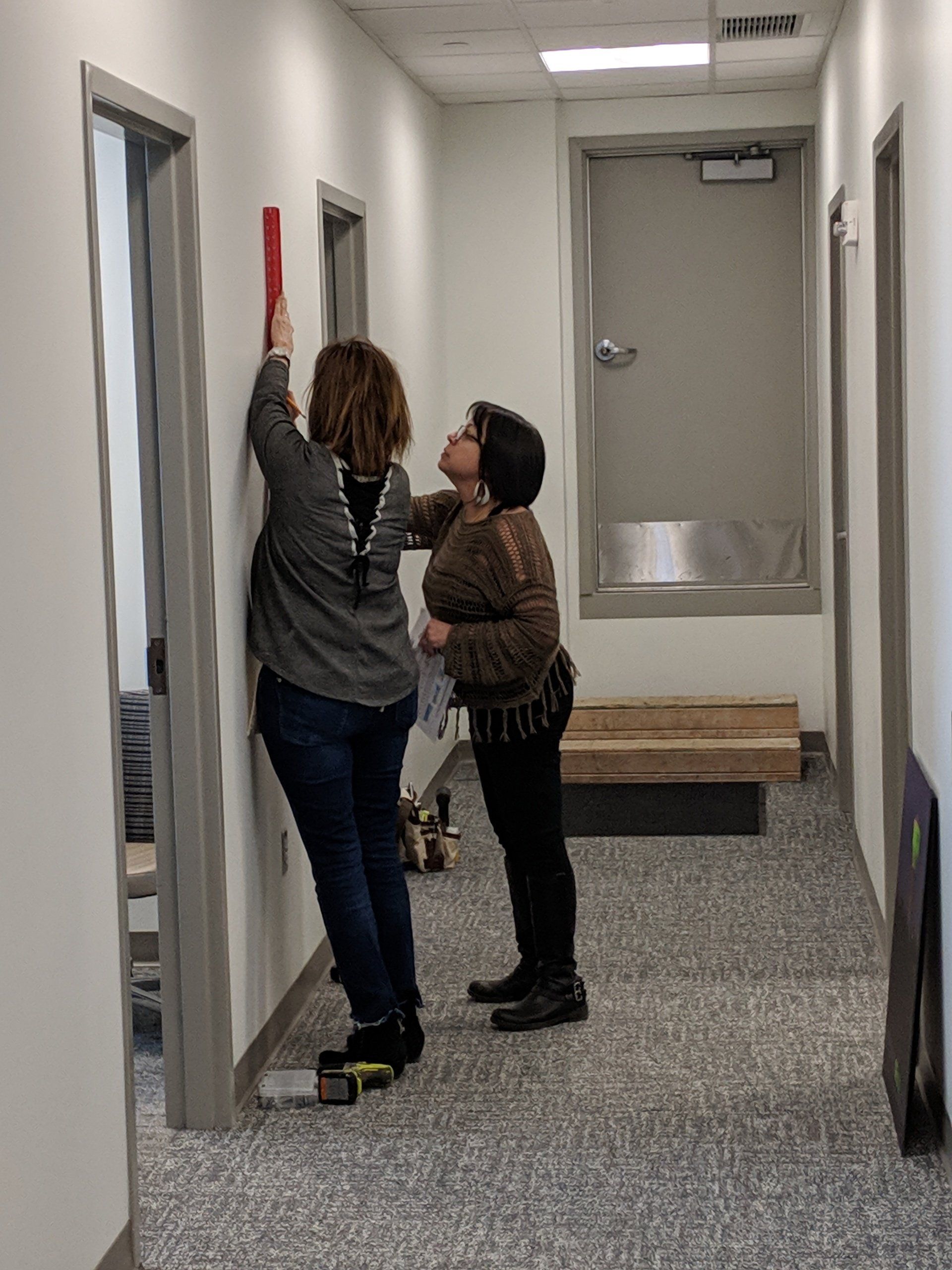 Two women are measuring a door in a hallway.