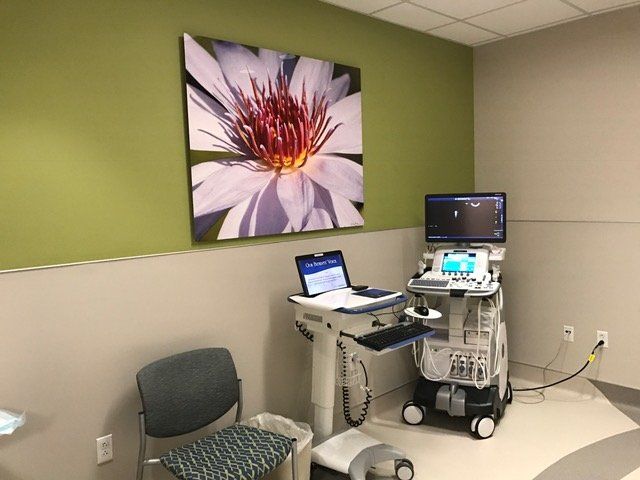 A room with a laptop on a desk and an ultrasound machine.