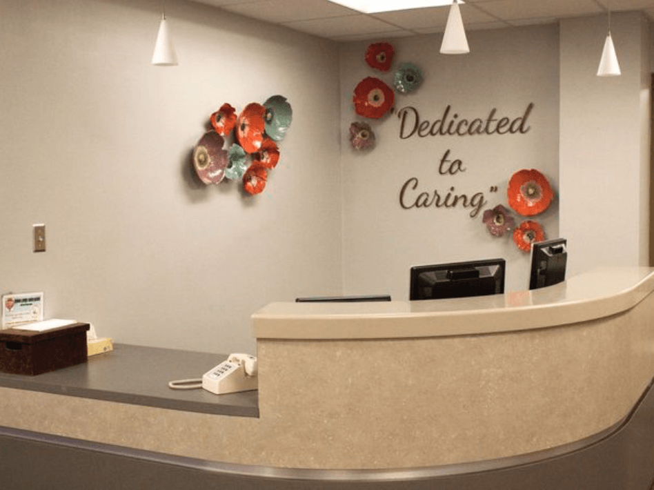 A reception desk with a sign on the wall that says dedicated to caring