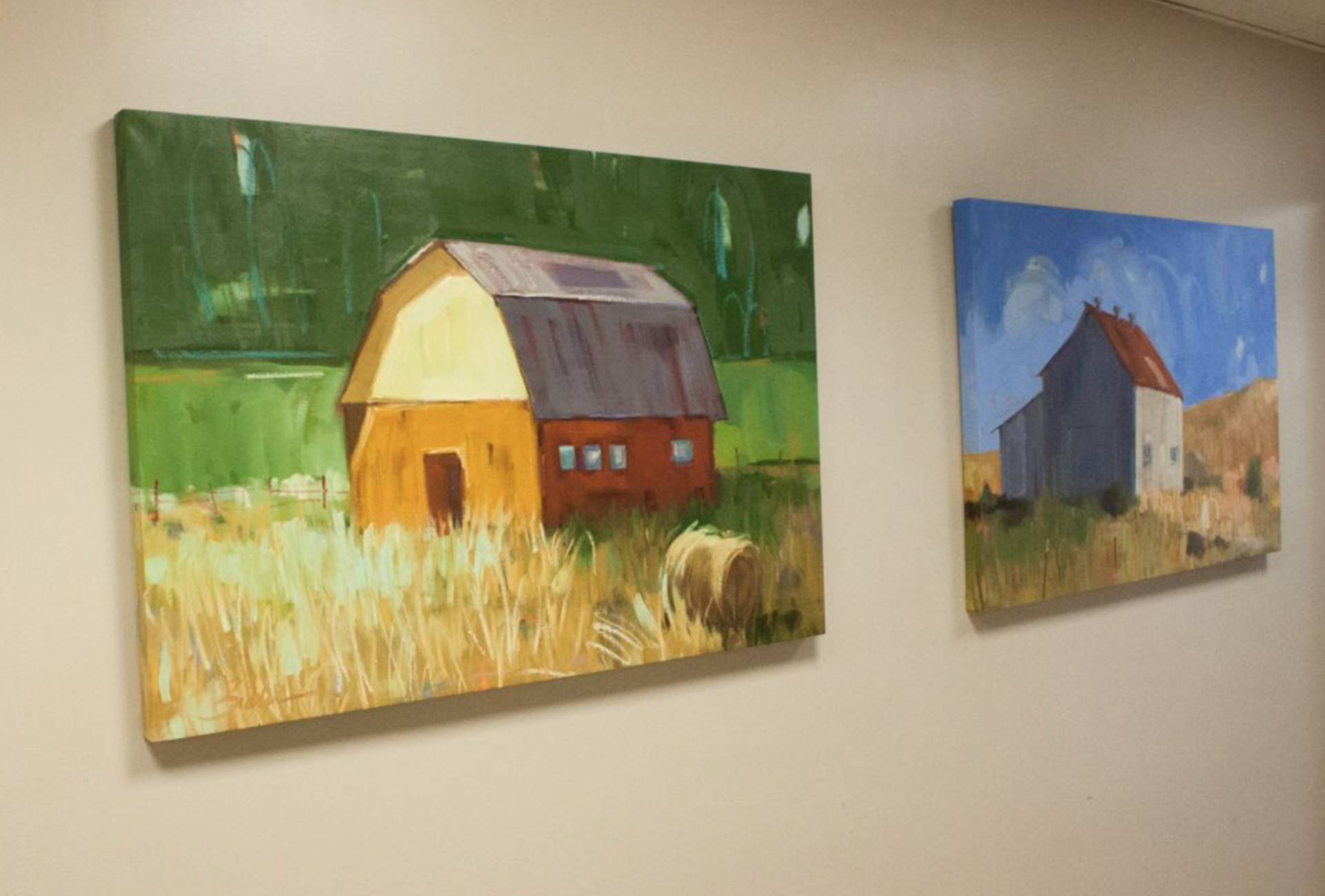 Two paintings of barns are hanging on a wall.