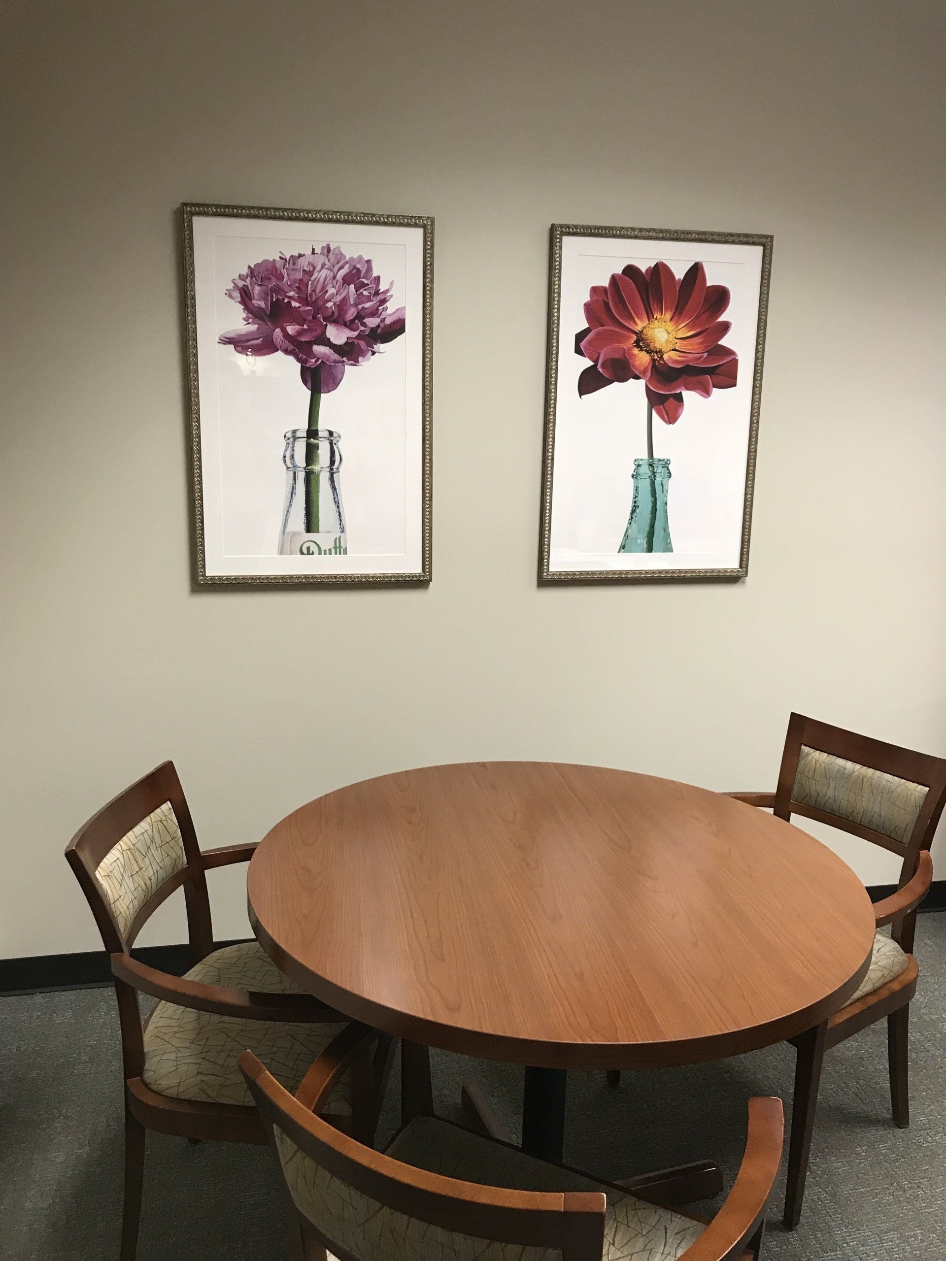 A room with a round table and chairs and two paintings of flowers on the wall