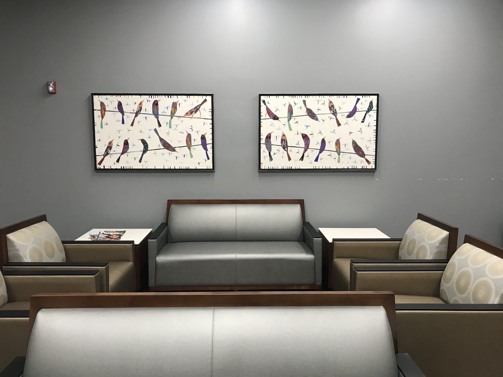 A waiting room with a couch and chairs and two paintings on the wall.