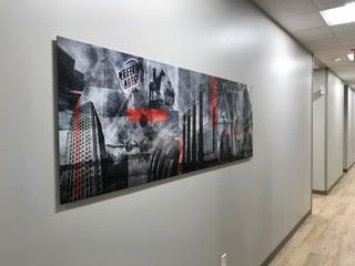 A long painting is hanging on a wall in a hallway.
