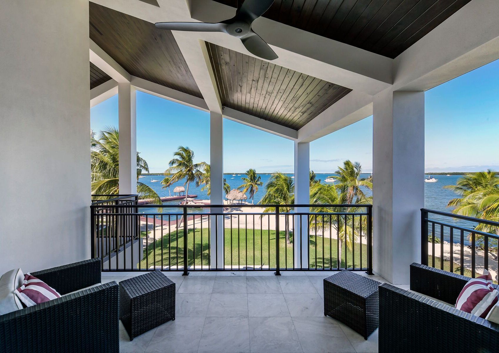 A balcony with chairs and a ceiling fan overlooking the ocean.