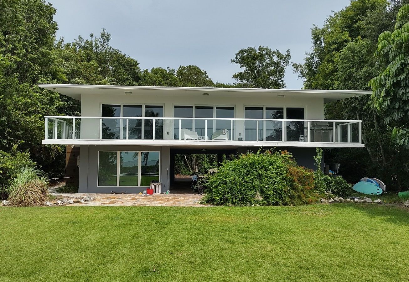 A white house with a balcony is surrounded by trees