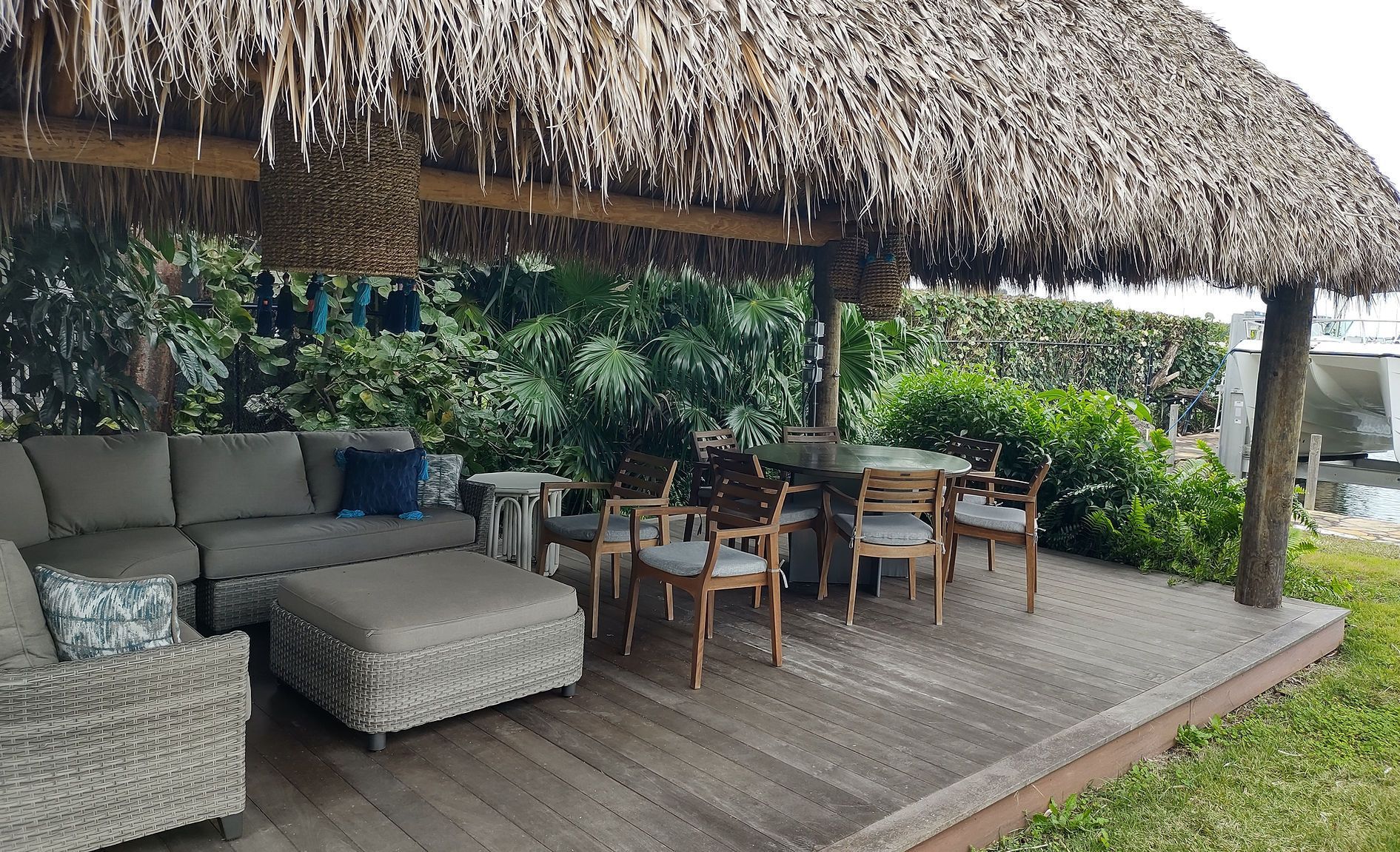 A wooden deck with a couch , chairs , and a table under a thatched roof.