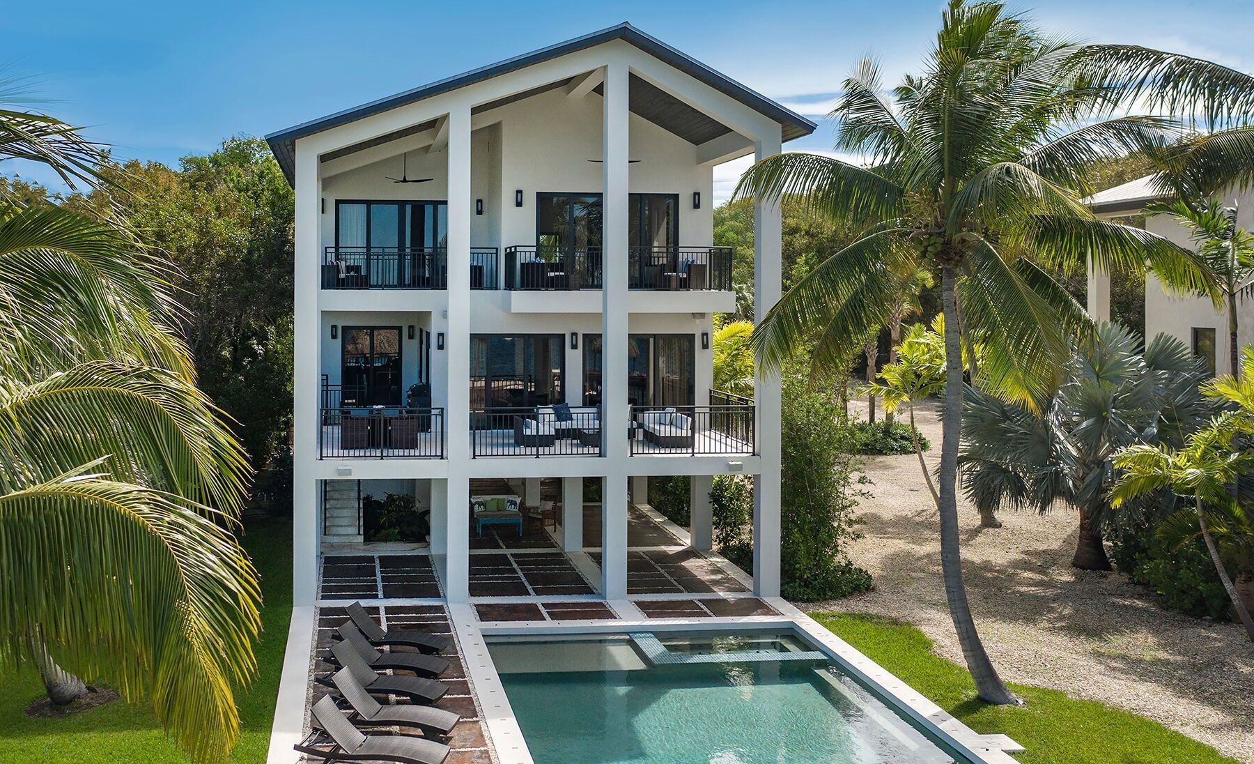 An aerial view of a large white house with a swimming pool surrounded by palm trees.