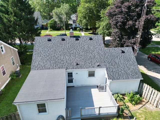 Aerial view of a house with a grey shingle roof, deck, and surrounding trees.