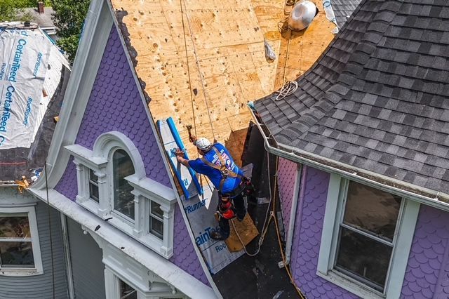 A man is working on the roof of a purple house.
