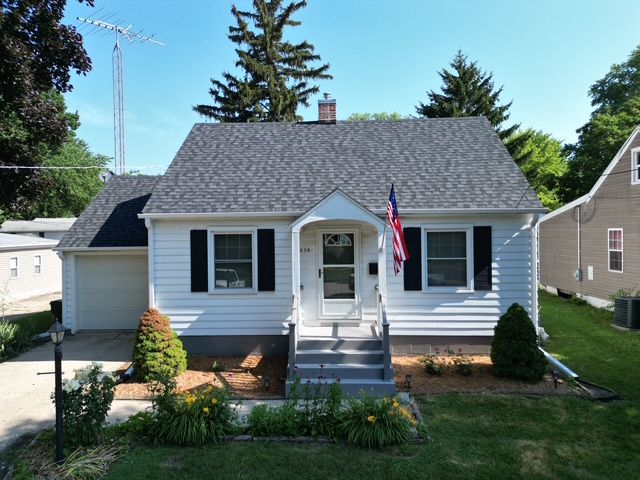 White house with black shutters, front porch, American flag. Green lawn, blue sky.