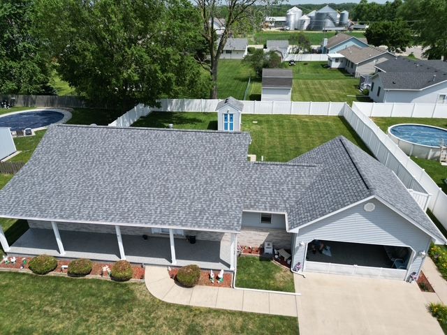 An aerial view of a light blue house with a gray roof, white fence, and two pools in a yard.