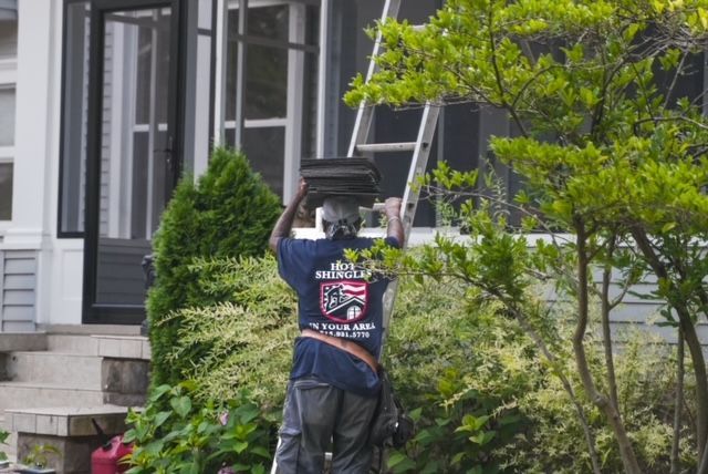 A man in a blue shirt is standing in front of a house with a ladder.