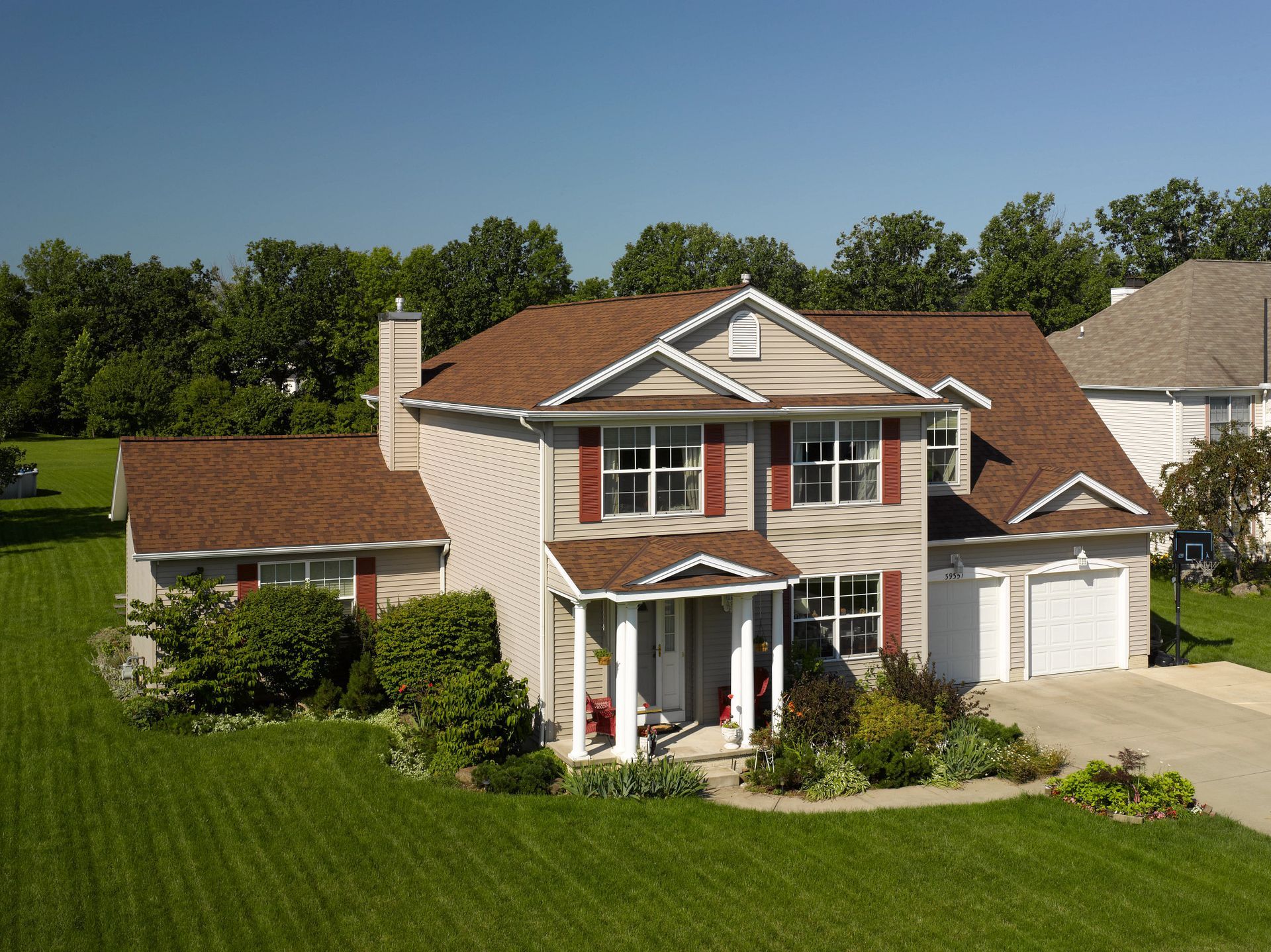 Two-story house with brown roof, beige siding, red shutters, and green lawn.
