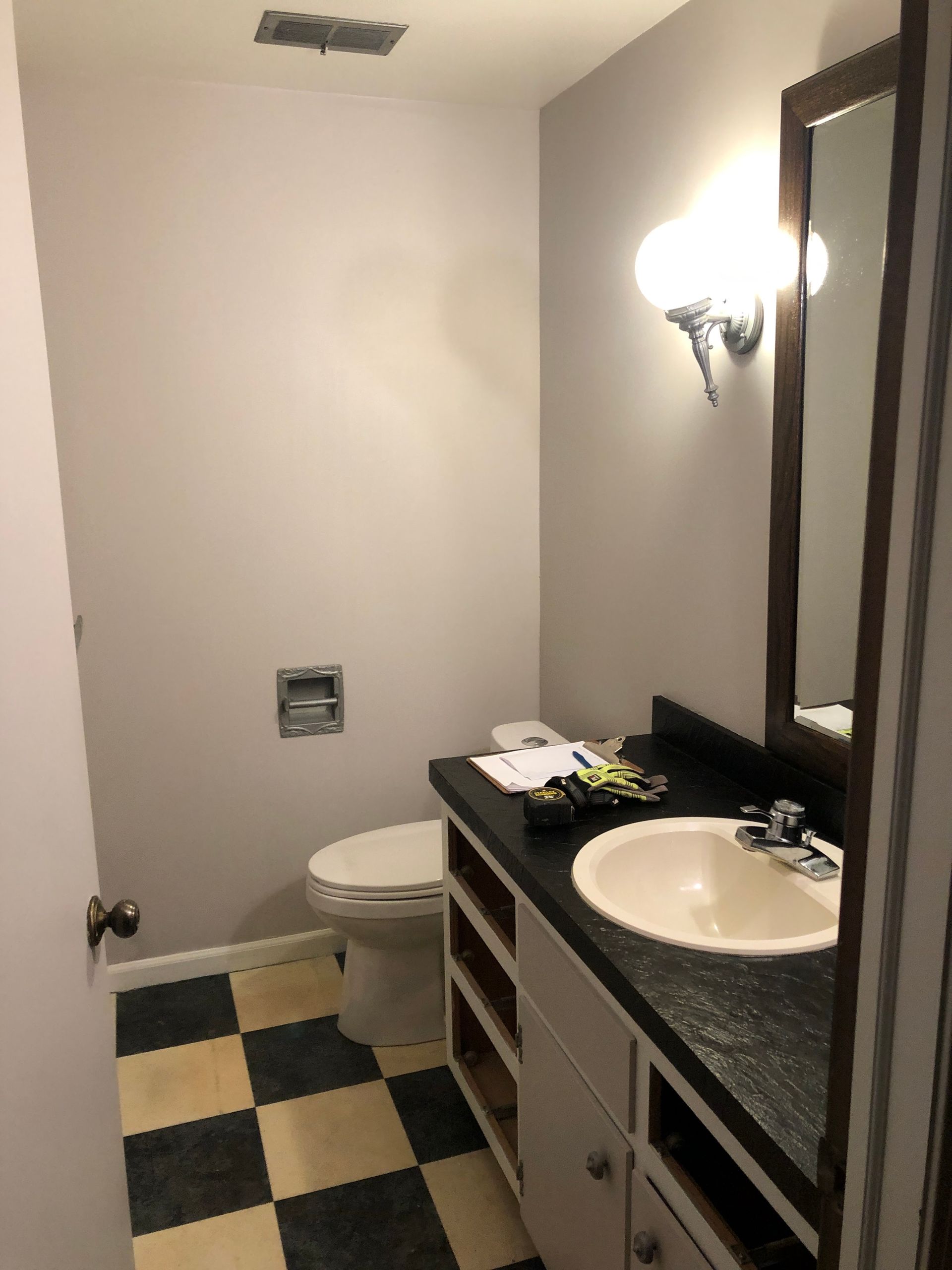 A bathroom with light grey walls, a black vanity, a white sink, a mirror, and a black-and-white checkered floor.