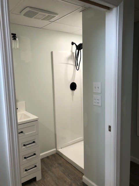 A modern bathroom featuring a white vanity with drawers, a walk-in shower with black fixtures, and light grey walls.