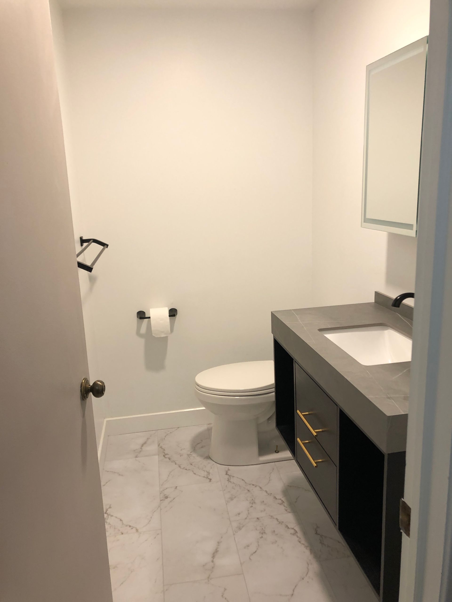 A modern bathroom with a white toilet, gray floating vanity, rectangular mirror, and white marble-patterned flooring.