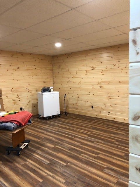 A room with wood-paneled walls, dark wood-look flooring, a white chest freezer, and a table with items on it.