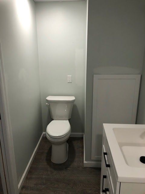 A white toilet in a small alcove next to a bathroom vanity with a white cabinet door on the adjacent wall.