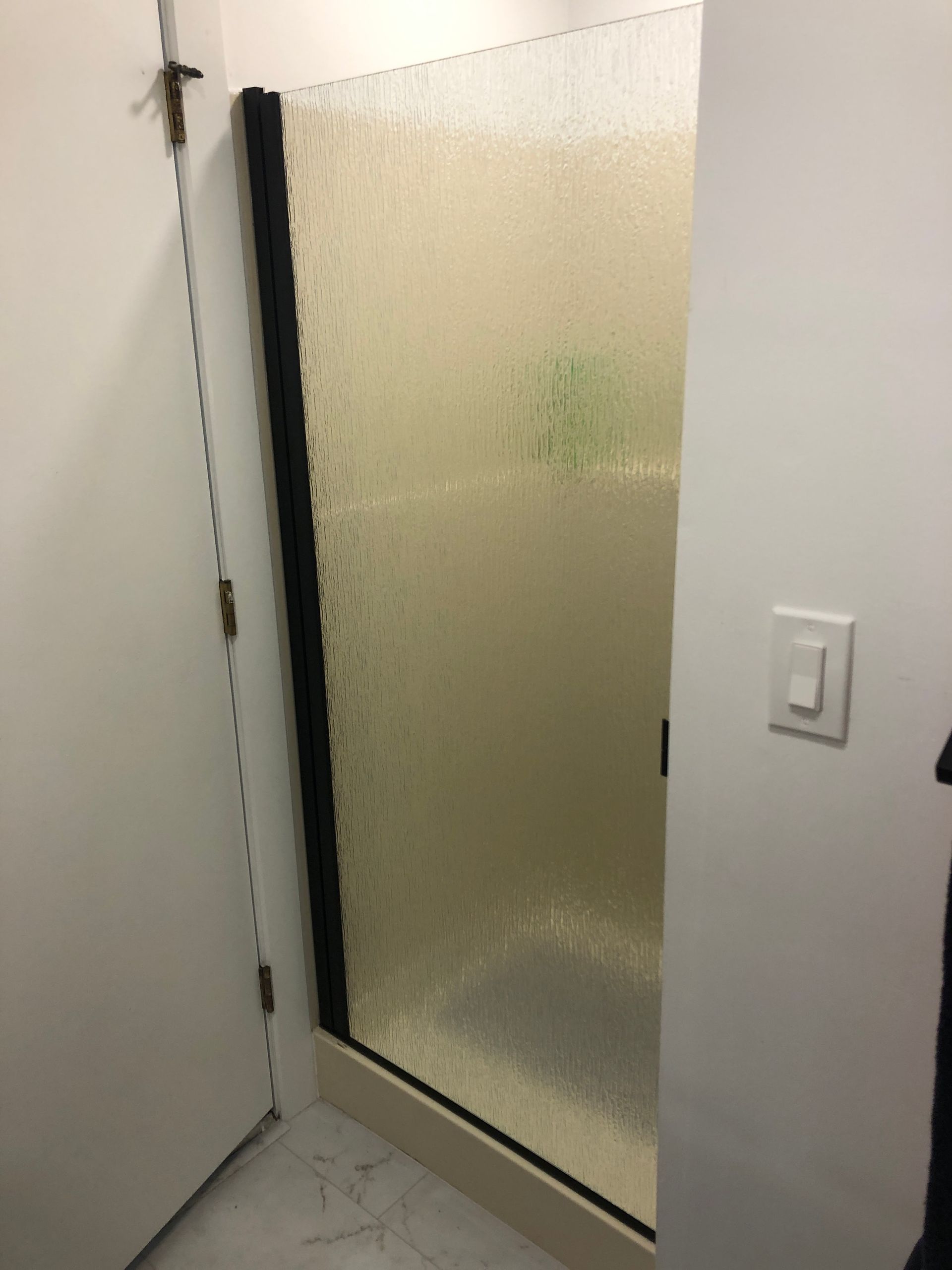 A shower enclosure with a textured glass door and black frame, set between white walls in a modern bathroom.