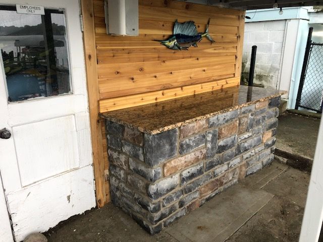 A stone bar with a granite top and wood paneling featuring a metal sailfish decoration, situated next to a white door.