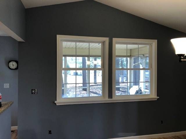 Two side-by-side white-framed windows set in a dark gray interior wall, with a partial view of a porch outside.