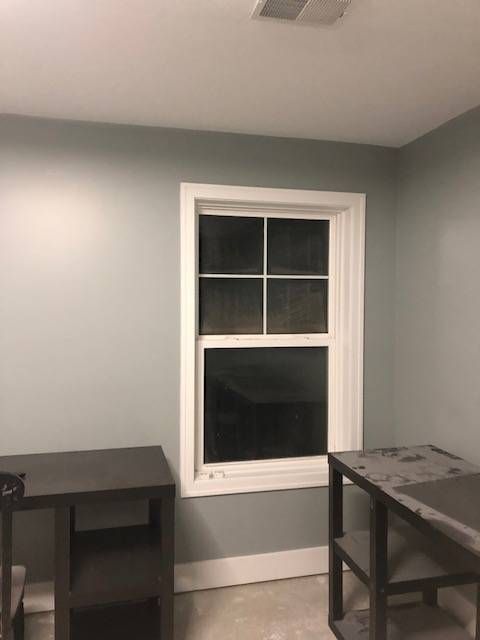 A window with white trim on a light gray wall, flanked by two dark storage units in a room.