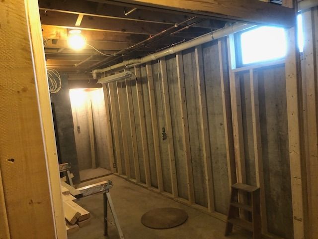 An unfinished basement featuring wooden wall studs, a concrete floor, a small window, and a wooden step stool.