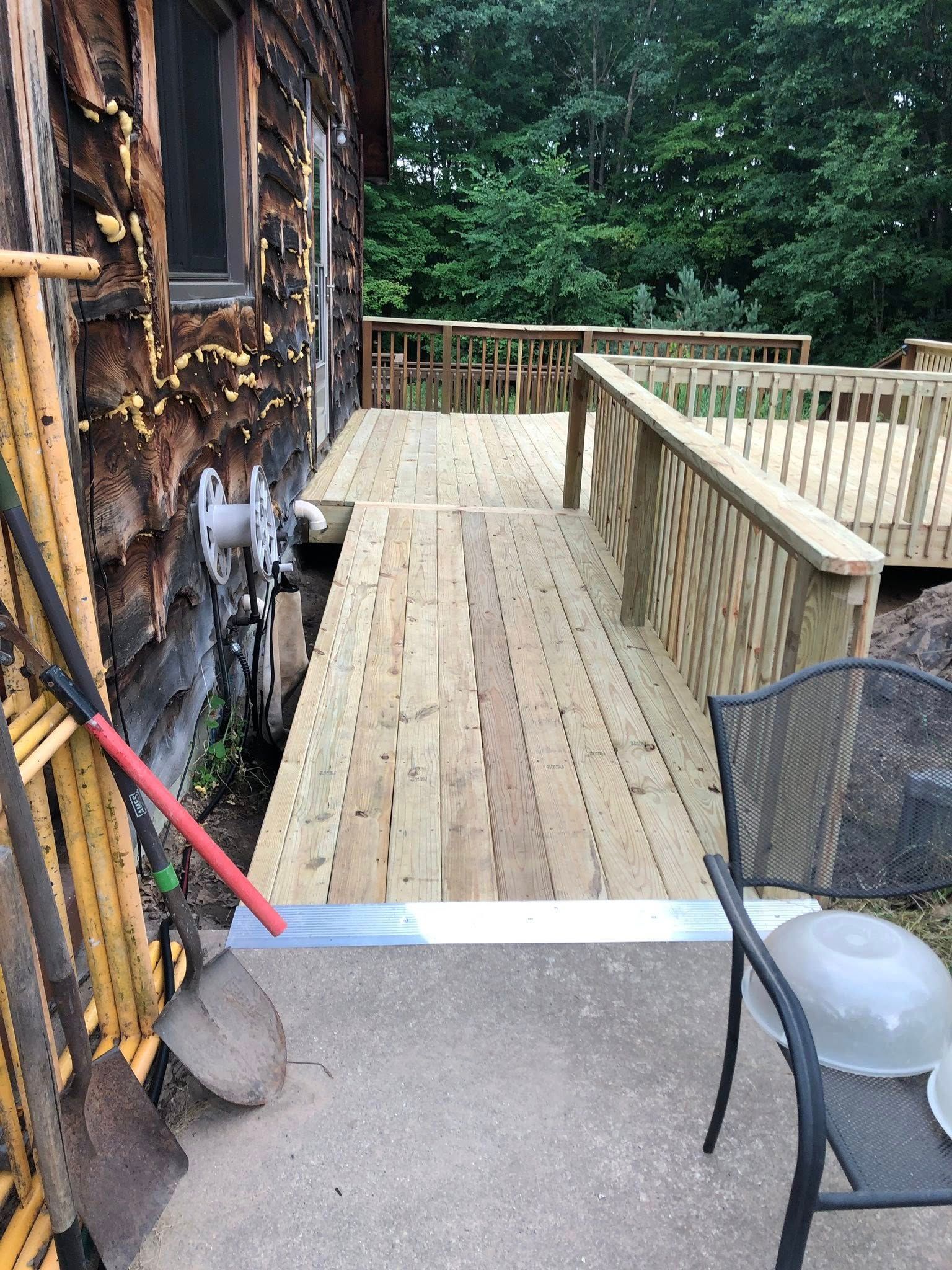 A wooden wheelchair ramp extending from a house to a deck, with a metal threshold transition to a concrete patio.
