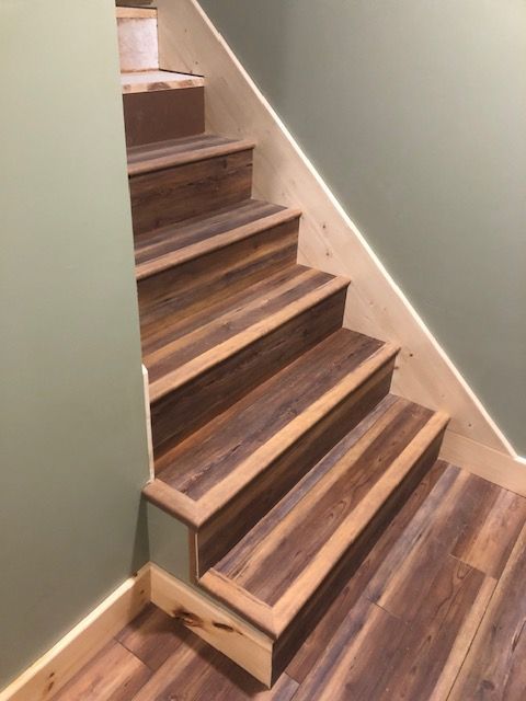 Wooden staircase with brown faux-wood vinyl flooring and unfinished light wood nosing against light green walls.