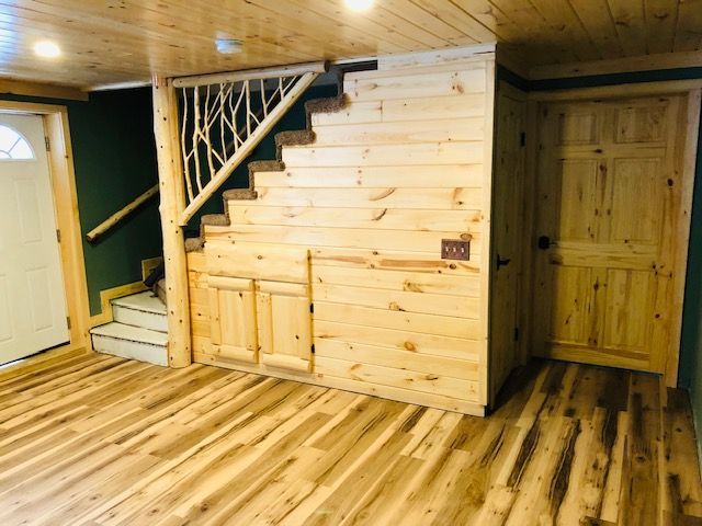 Wooden stairs with twig-style railing beside a storage closet and closed doors in a room with light wood-plank flooring.