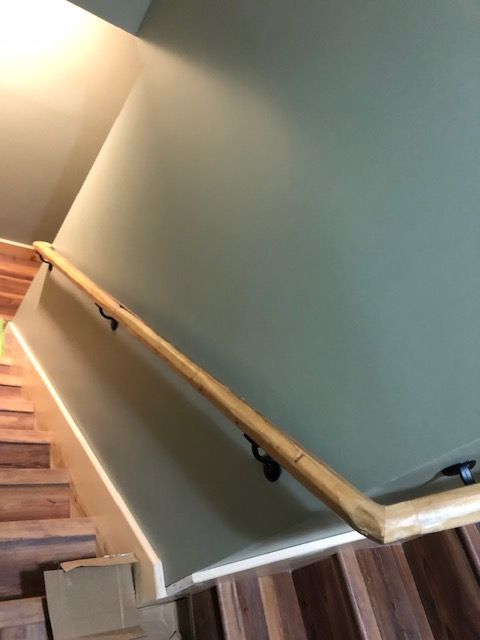 A wooden handrail mounted on a sage green wall running alongside a wooden staircase.