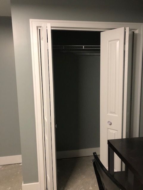 A white bi-fold closet door standing partially open in a room with light blue-gray walls.