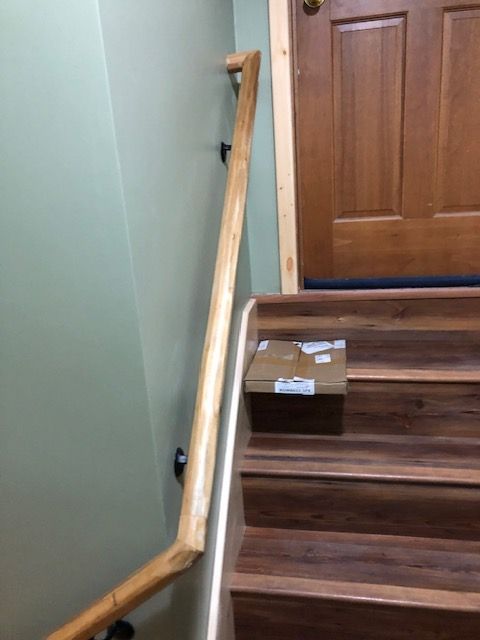 A wooden handrail follows the angle of a wooden staircase, with a small package sitting on one of the steps.