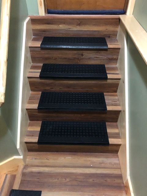 A short wooden staircase featuring four steps with black rubber tread mats, framed by beige walls and a handrail.