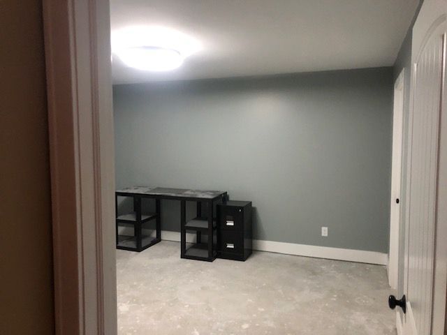 A view into a room with gray walls, a light-colored concrete floor, a black desk, and a matching black filing cabinet.