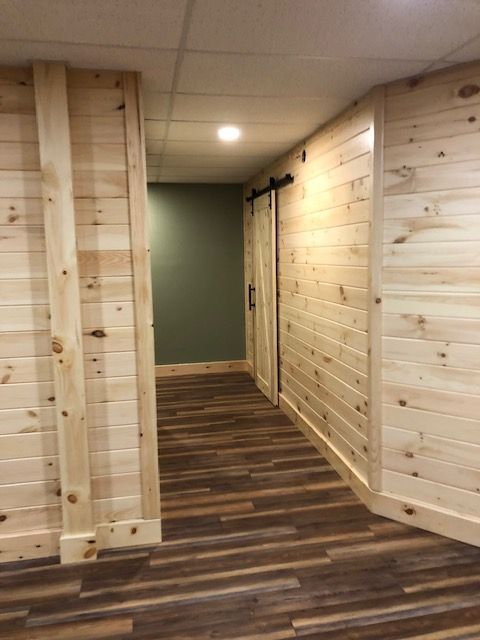 A hallway featuring light wood paneling on the walls, dark wood-look floors, and a barn door leading to a green-walled room.