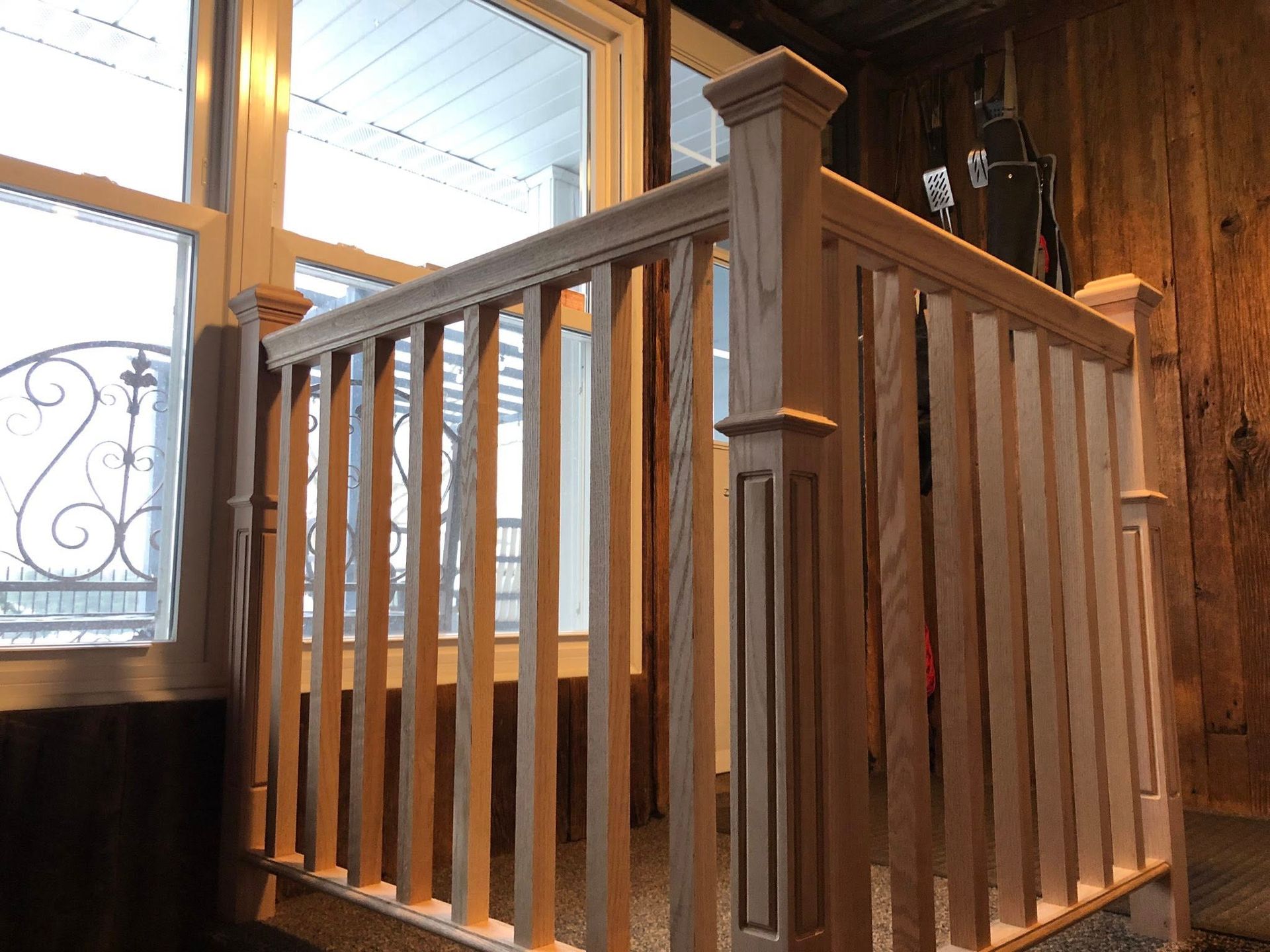 A light-colored wooden staircase railing and square newel posts stand in front of a window indoors.