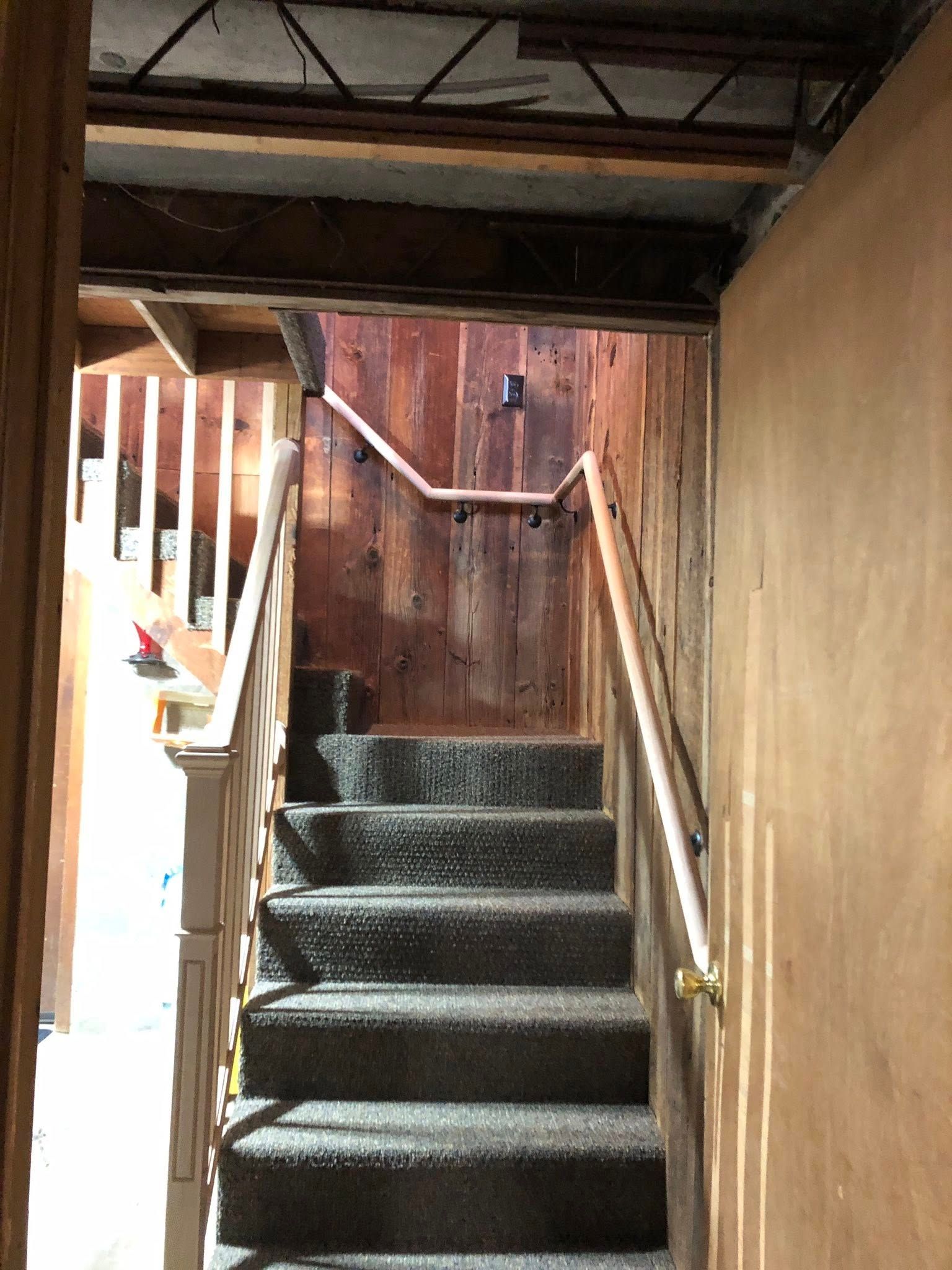 A carpeted staircase leads upward to a wood-paneled landing between two railings.