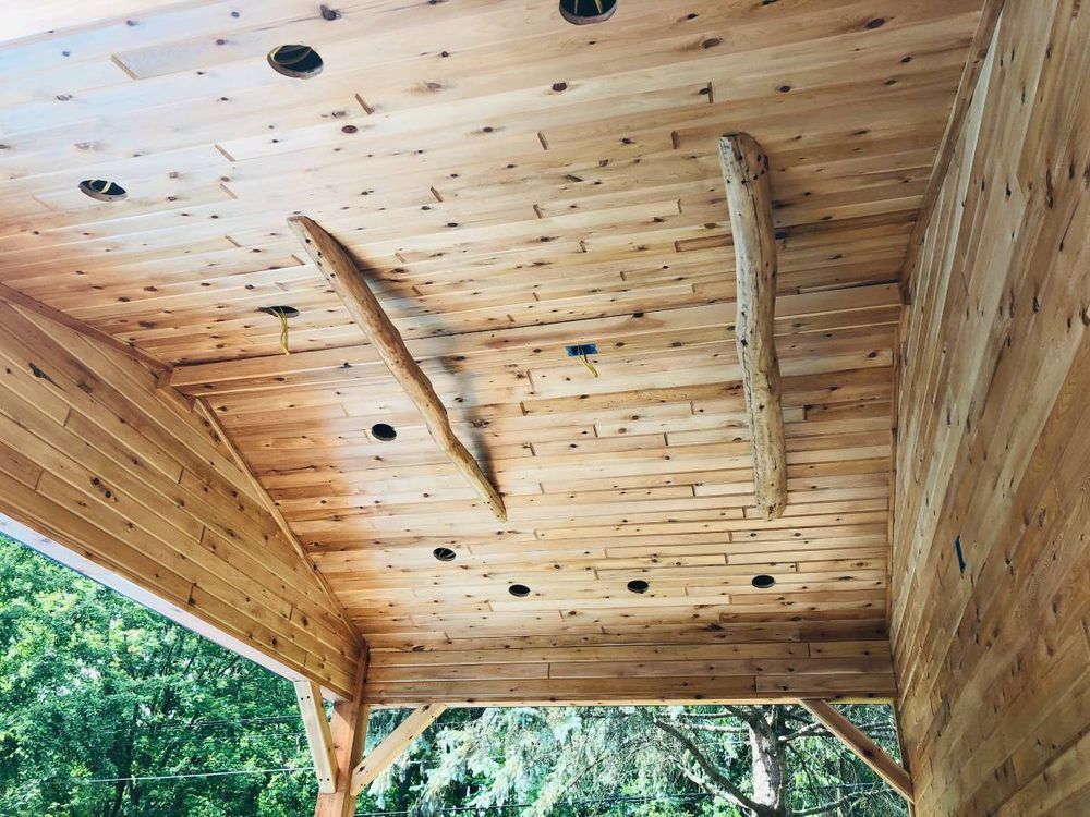 Wood-paneled ceiling with two natural log beams and recessed lighting, viewed from beneath a covered porch.