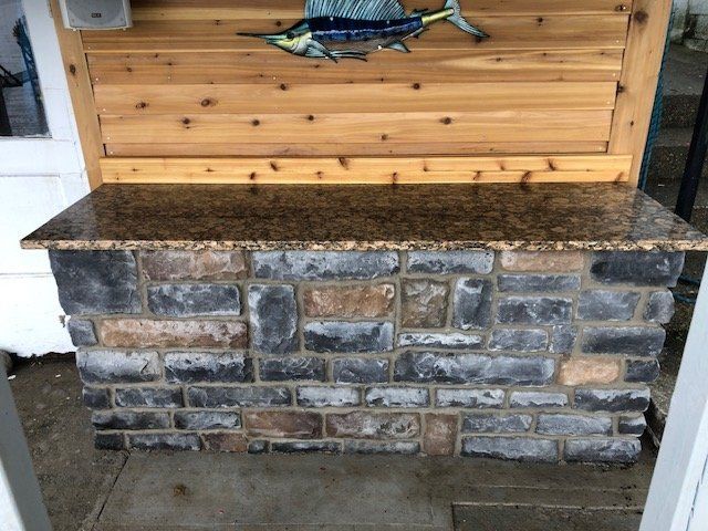A stone bar with a polished brown countertop set against a wood-paneled wall decorated with a metal marlin wall art piece.