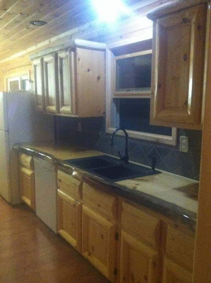 A rustic kitchen with wood cabinets, live-edge countertops, a black sink, and light wood walls.