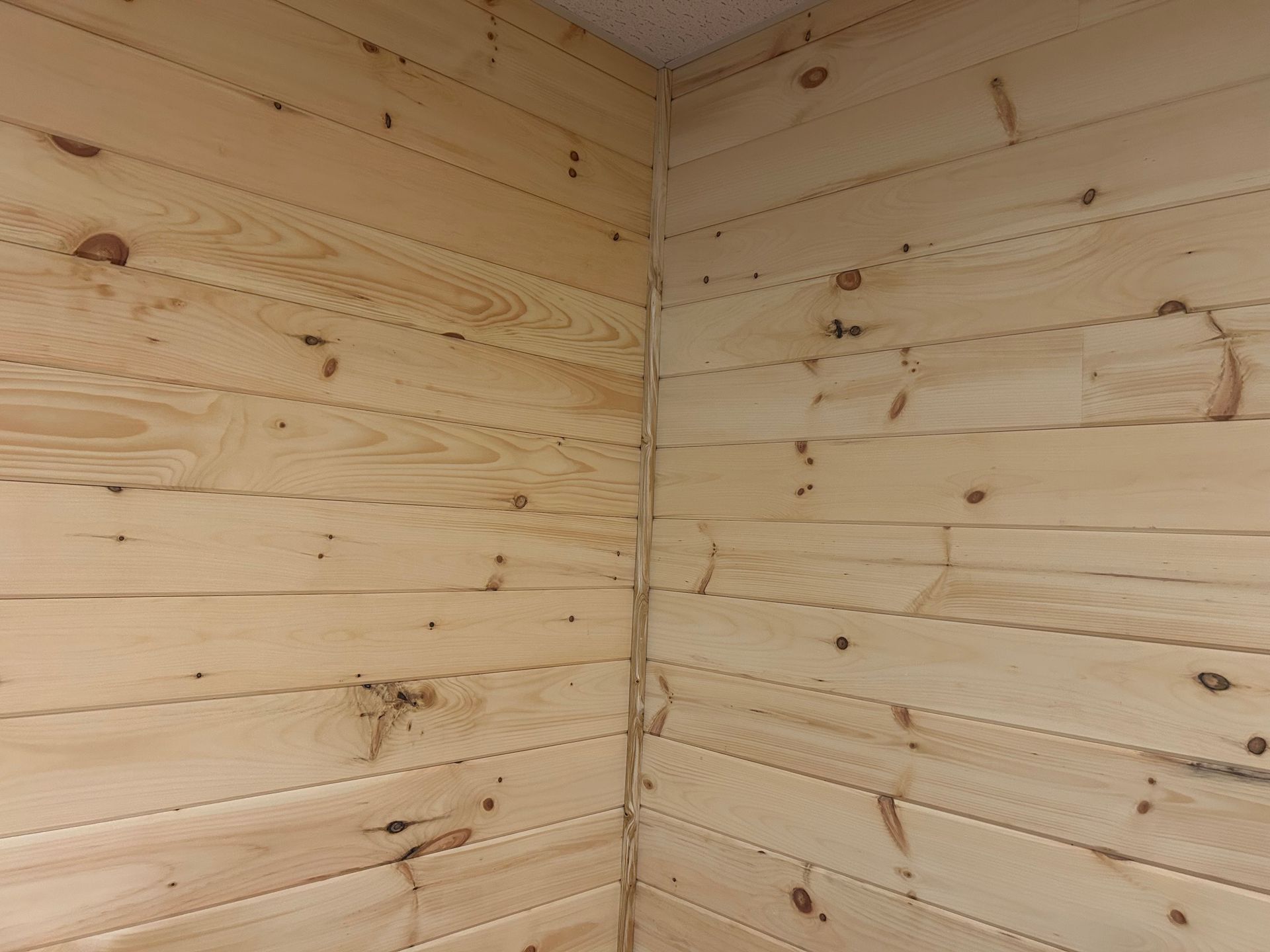 An interior corner where two walls meet, covered in horizontally installed light-colored pine wood planks.