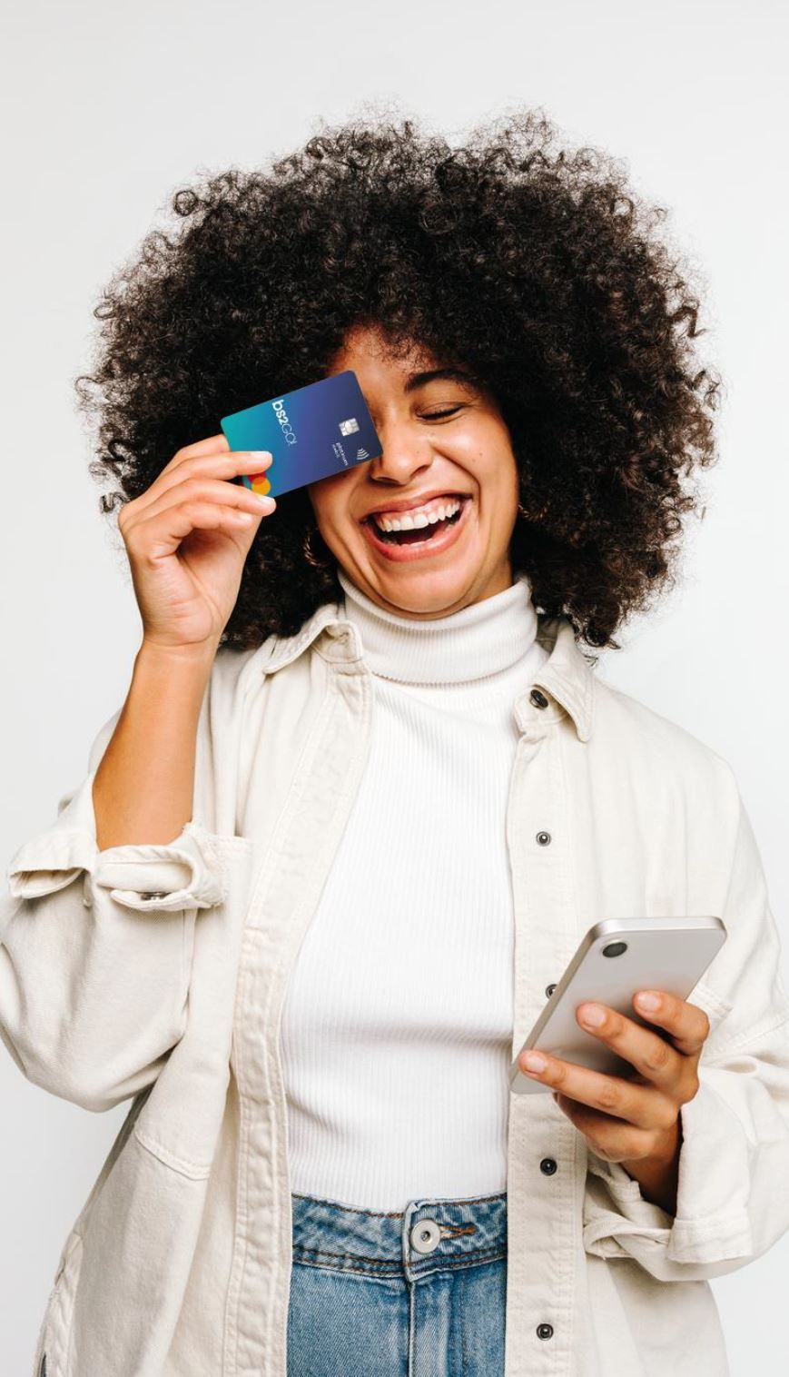 uma mulher segura um cartão de crédito diante dos olhos e usa um telefone celular.
