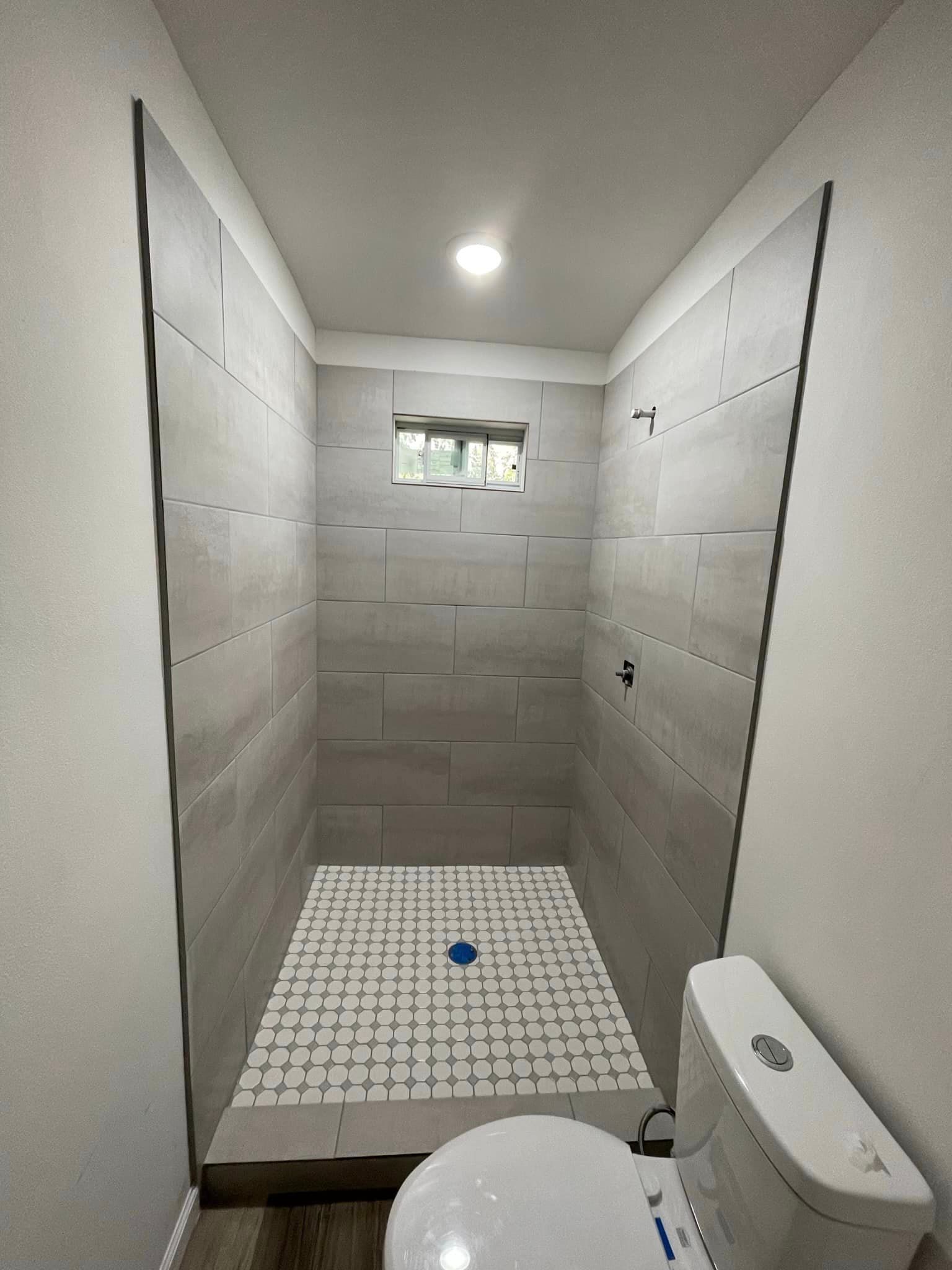 A bathroom with a toilet , shower , and window.