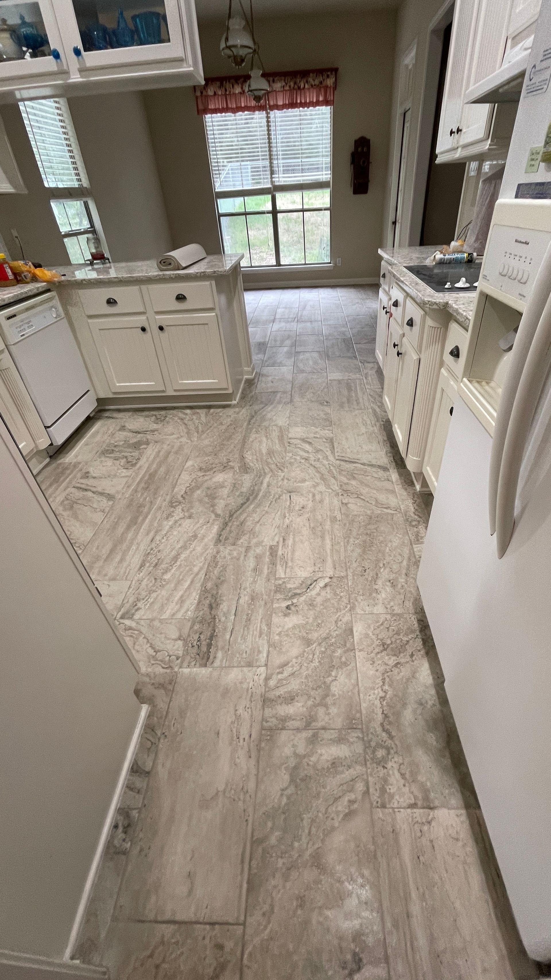 A kitchen with white cabinets , a refrigerator , a sink , and a window.