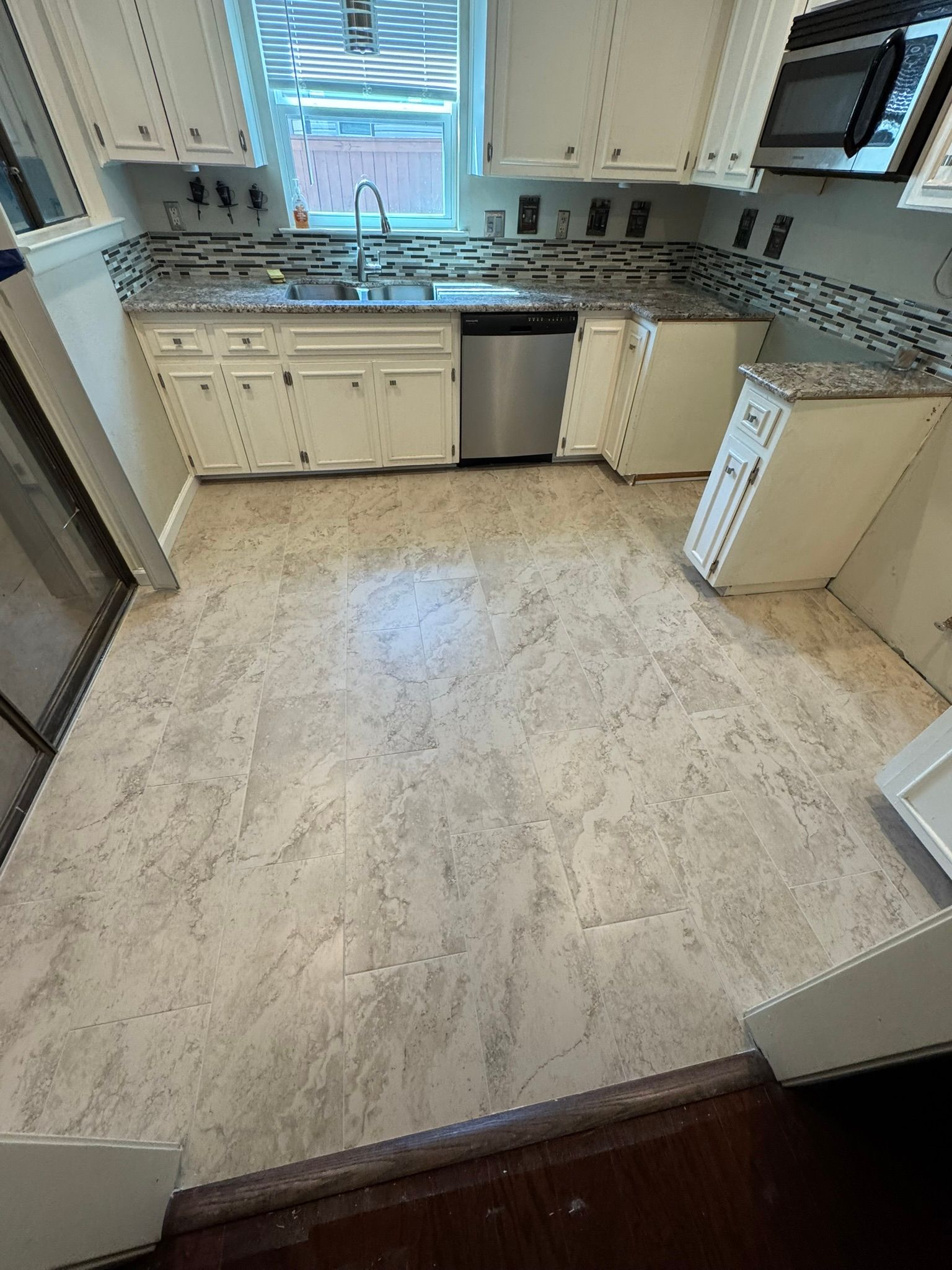 A kitchen with white cabinets and a marble floor.