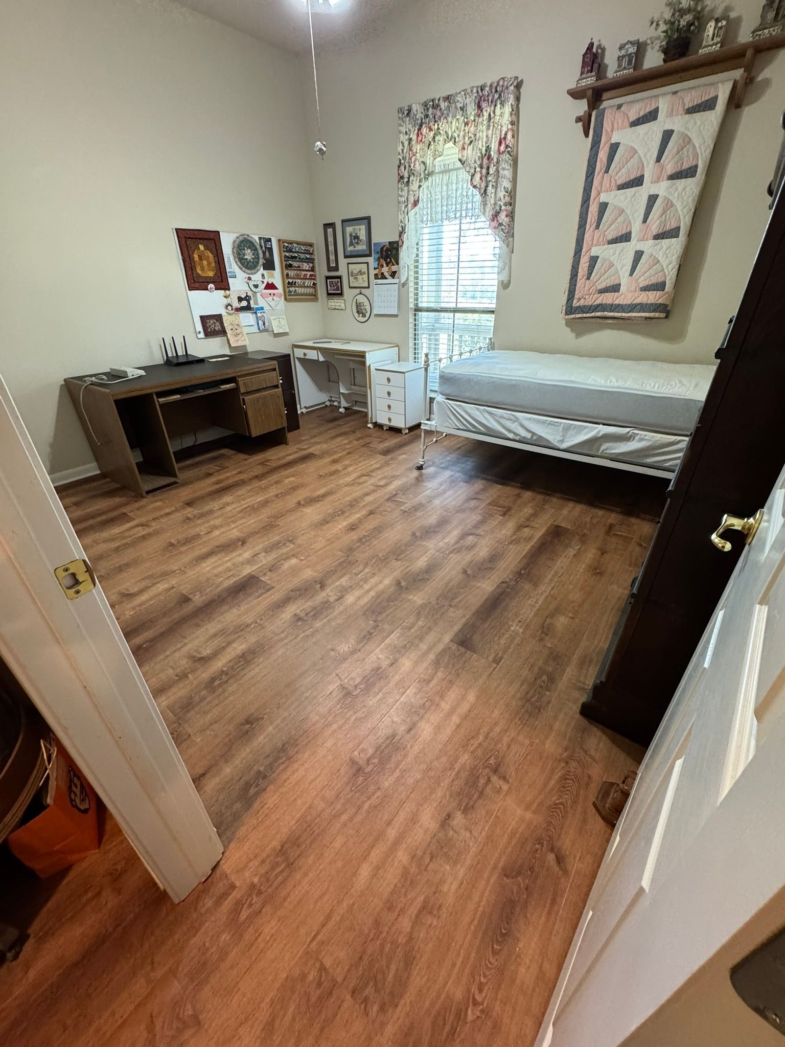 A bedroom with hardwood floors , a bed , a desk , and a window.