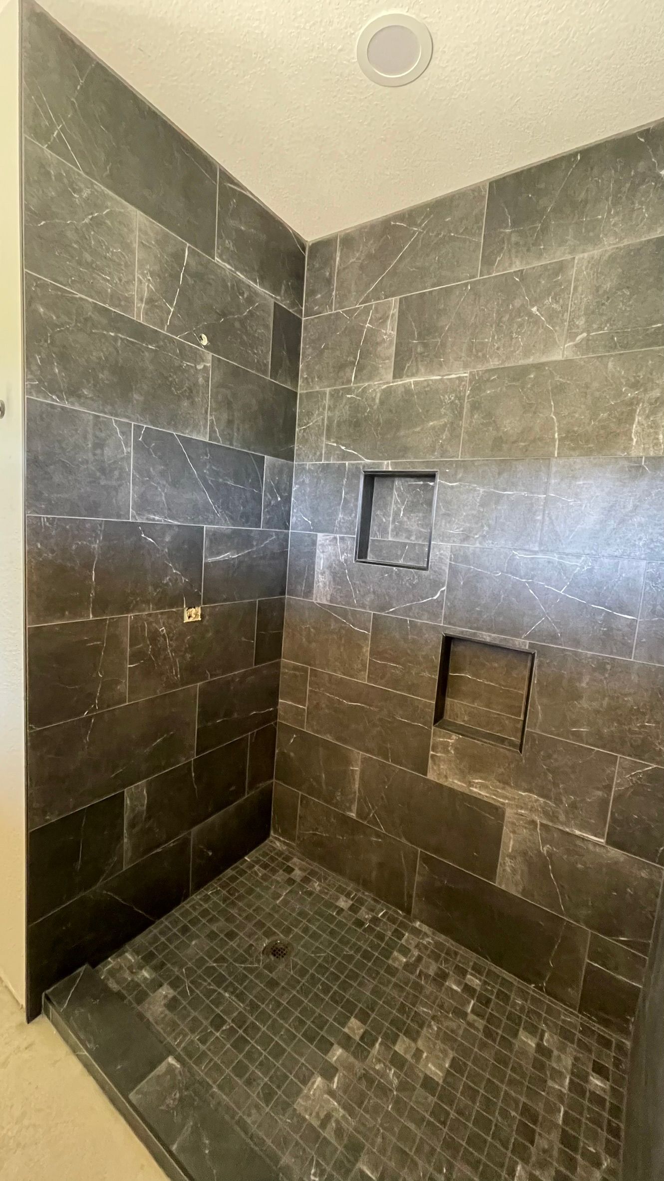 A walk in shower with black tiles and a niche in the wall.